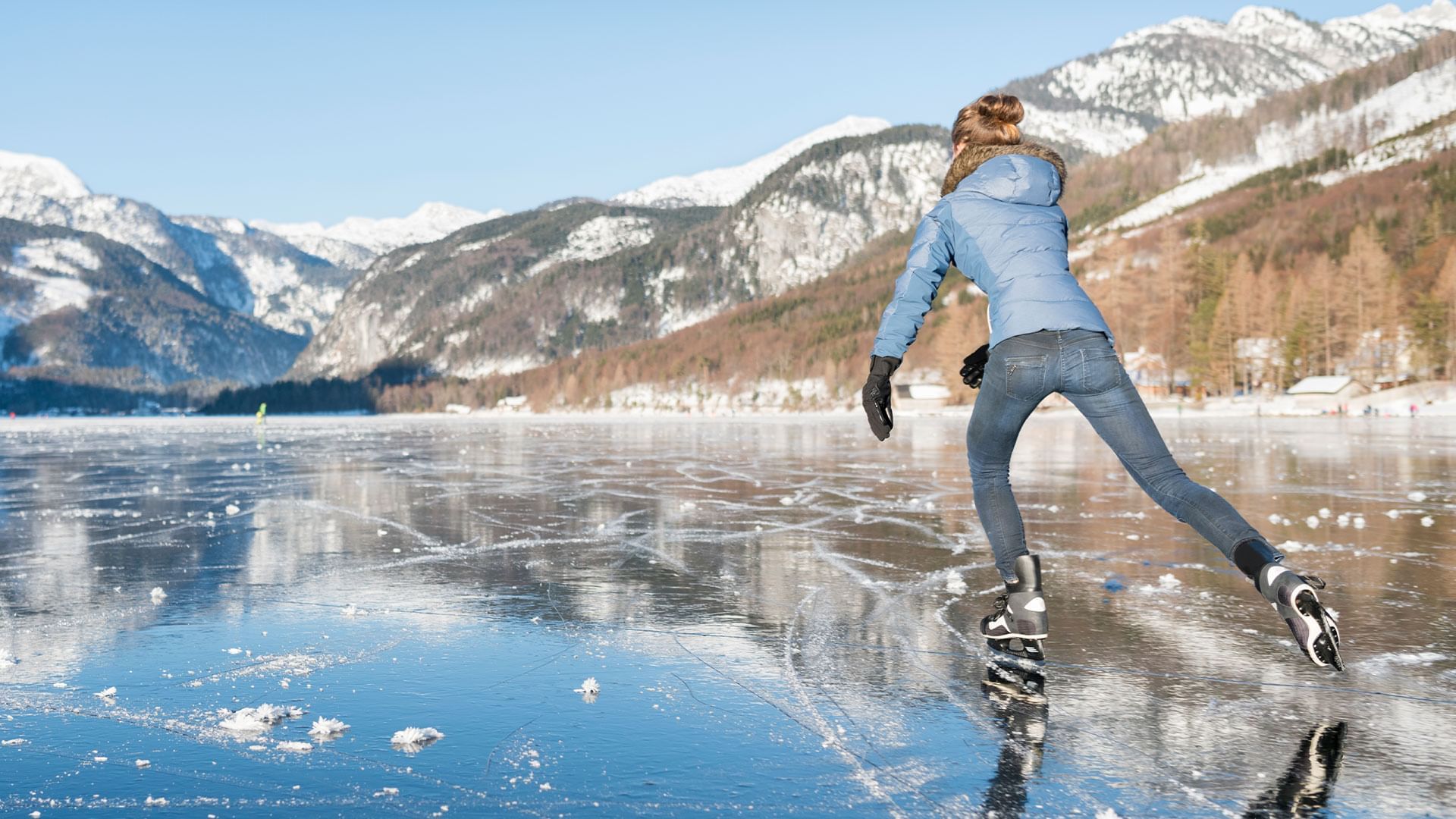 Ice skater on a frozen lake with snow-capped mountain backdrop at Falkensteiner Hotels & Residences