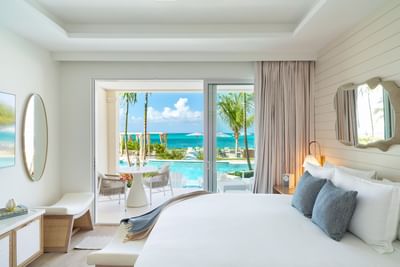 Ottoman, side cupboard, and nightstand by the bed in Two Bedroom Beachfront Pool Junior Suite at Windsong Resort On The Reef