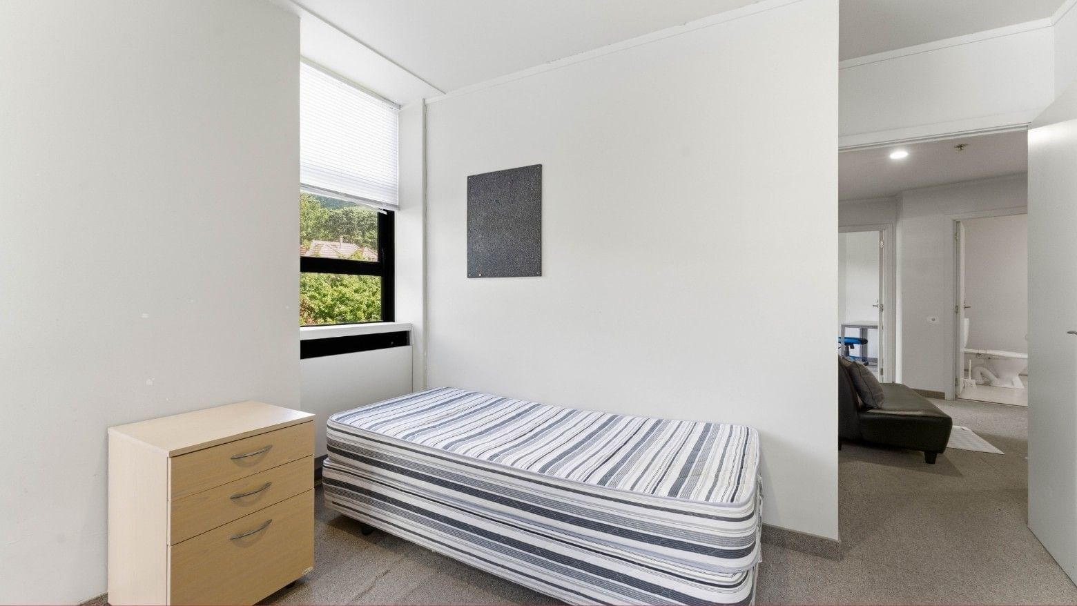 A small bedroom with a bed, dresser, and open door at UniLodge Stafford House.