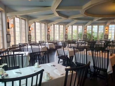 Seasons Restaurant with set tables and wooden chairs under geometric ceiling beams at Avon Old Farms Hotel