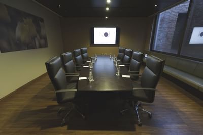 Mesa de reuniones con sillas de cuero bajo lámpara de techo frente a gran pantalla en Sala Florencia de NOI Vitacura