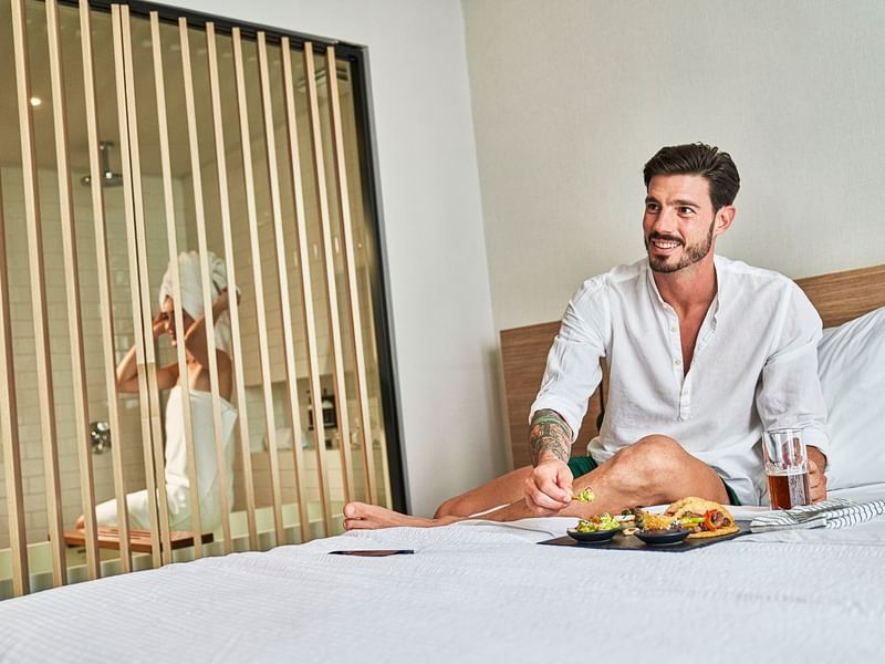 Man having meal on the bed, lady in the shower, IOH Hotels