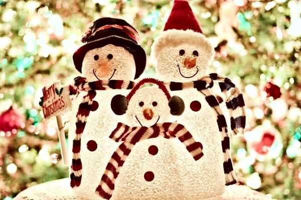 A family of smiling snowmen reflecting the glow of a bright Christmas tree.