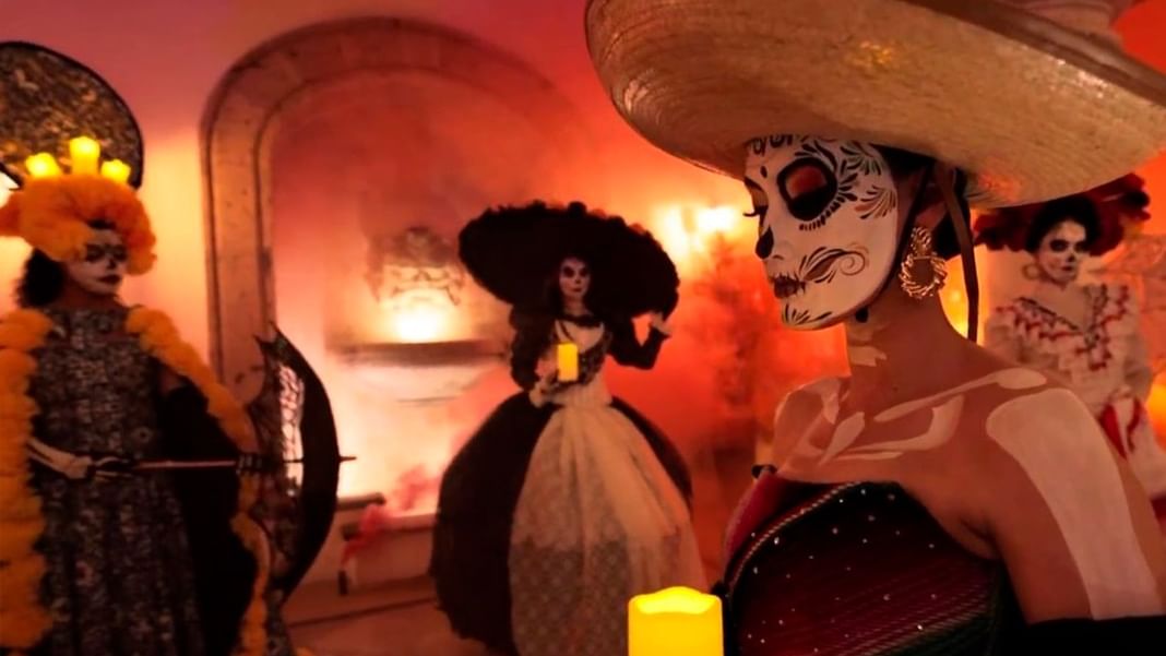 Personas con maquillaje de calavera y sombreros tradicionales en un Desfile de Día de Muertos con velas y ambiente cálido