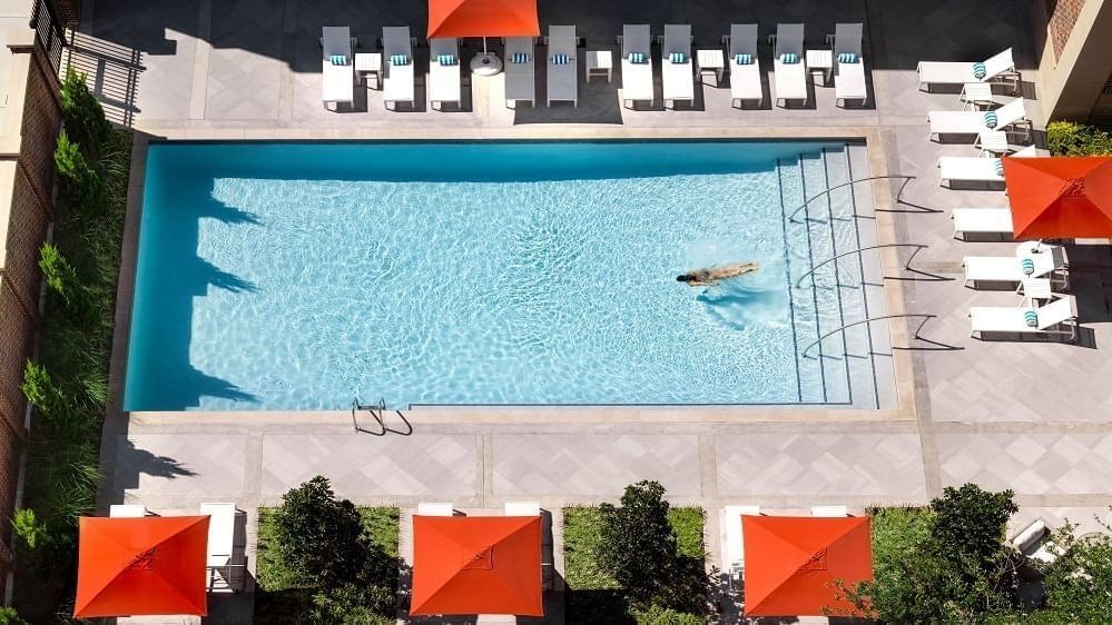 Blue pool by lounge chairs under orange umbrellas surrounding the outdoor deck at Warwick Melrose Dallas