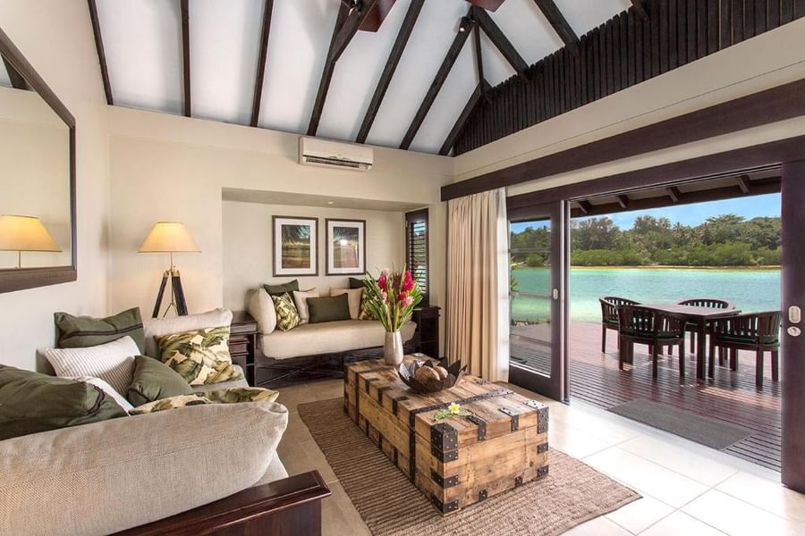 Tropical lounge with a wooden trunk table and open doors leading to a scenic pool deck at warwick le lagon-vanuatu