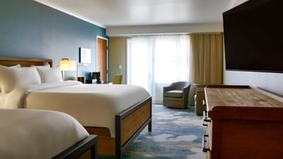 A bedroom at The Stanley Hotel with two queen beds, a blue wall, and a large window with sheer curtains