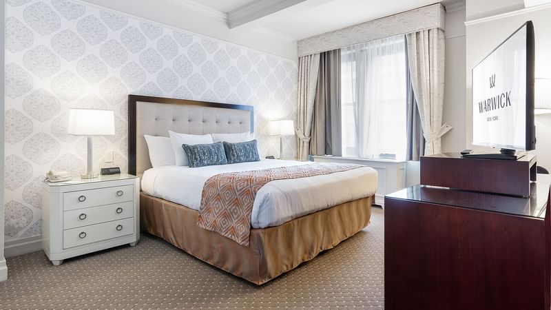 Cozy bed with side tables and working table in On The Avenue One Bedroom Suite at Warwick New York
