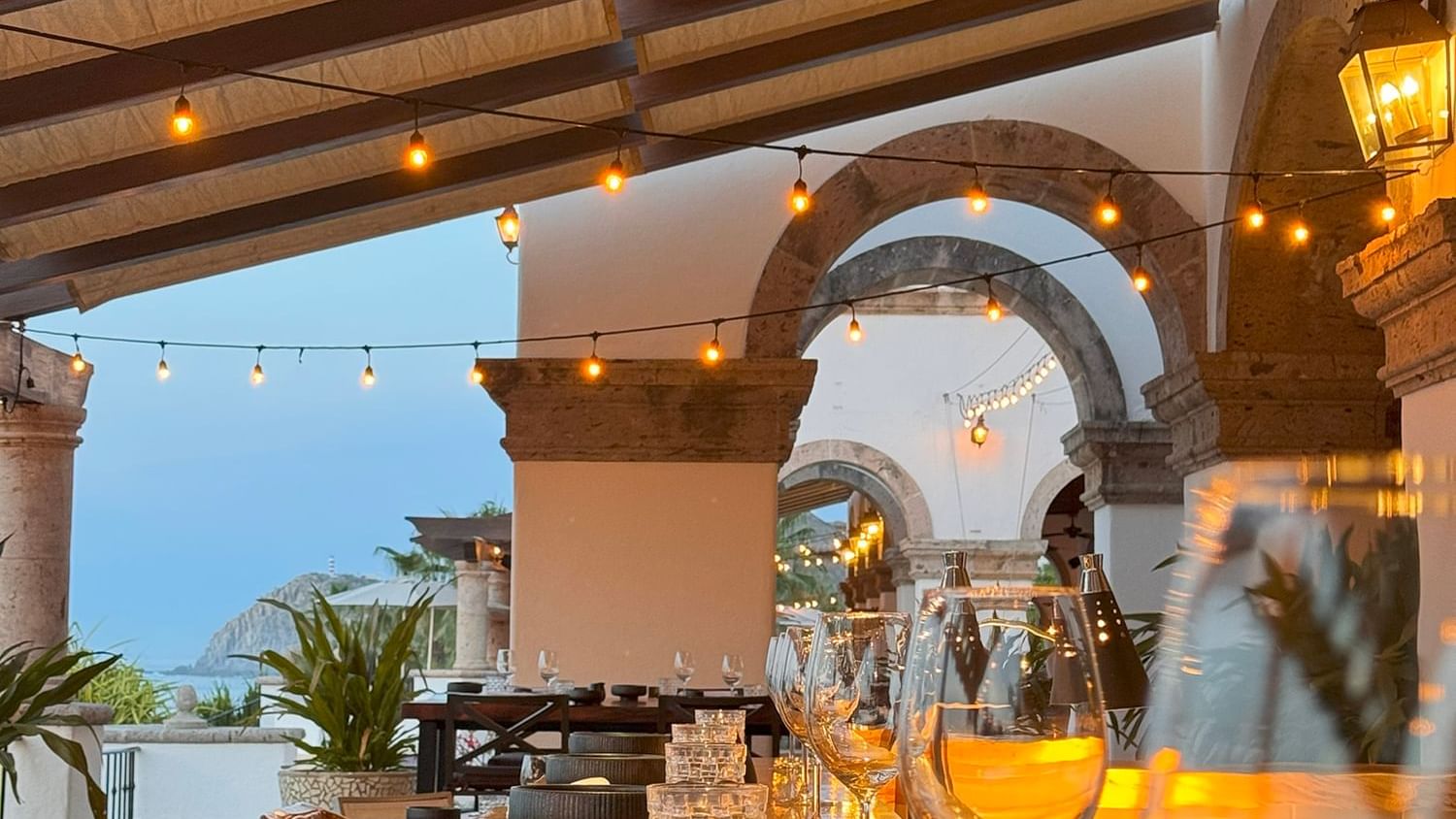 Comedor La Terraza del Santo con una mesa larga con cristalería y guirnaldas de luces en Hacienda del Mar Los Cabos
