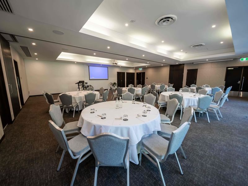 Temple Room with round tables, chairs & projector screen on the wall at Pullman Port Douglas