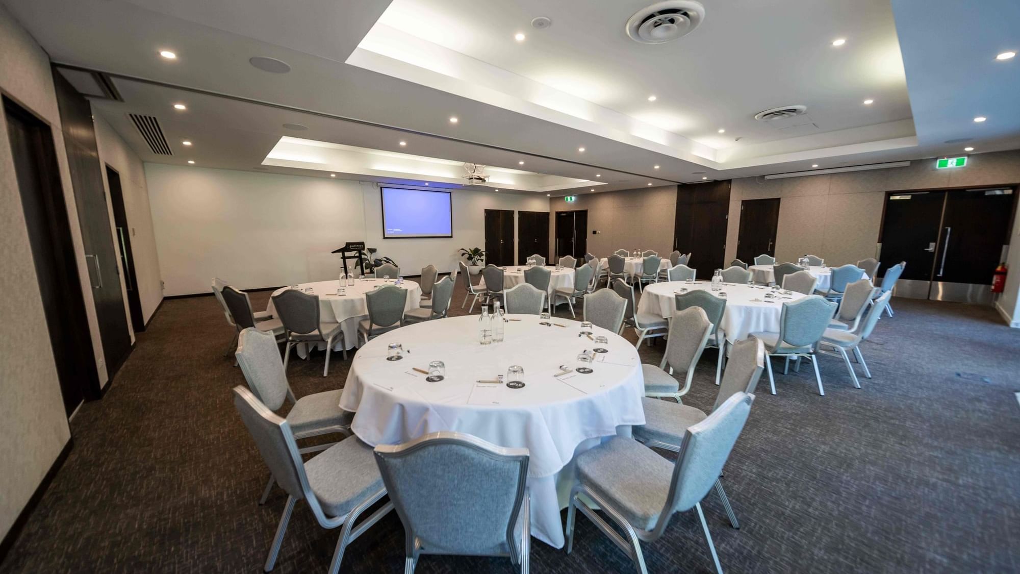 Temple Room with round tables, chairs & projector screen on the wall at Pullman Port Douglas