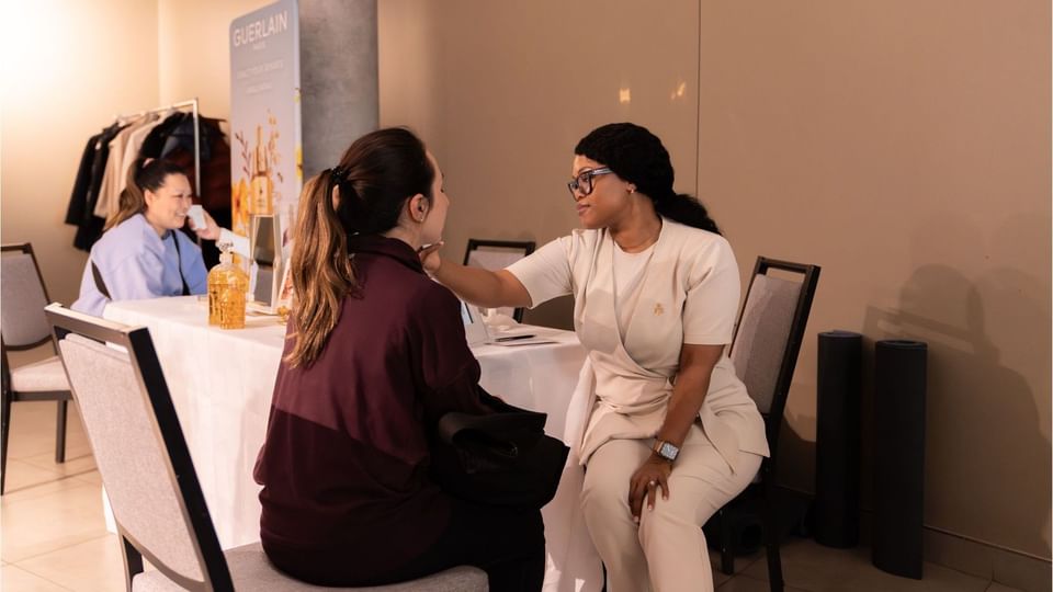Skincare specialist examining a seated guest by a Guerlain display under warm event lighting at Hotel X Toronto