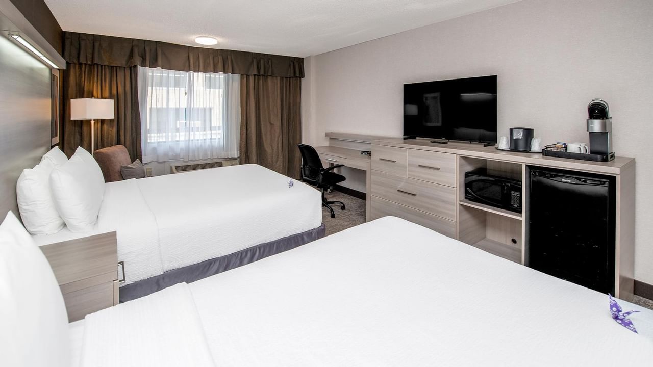 Modern double queen guest room with white bedding, work desk, flat-screen TV, and mini-fridge at Coast Calgary University Area Hotel by APA