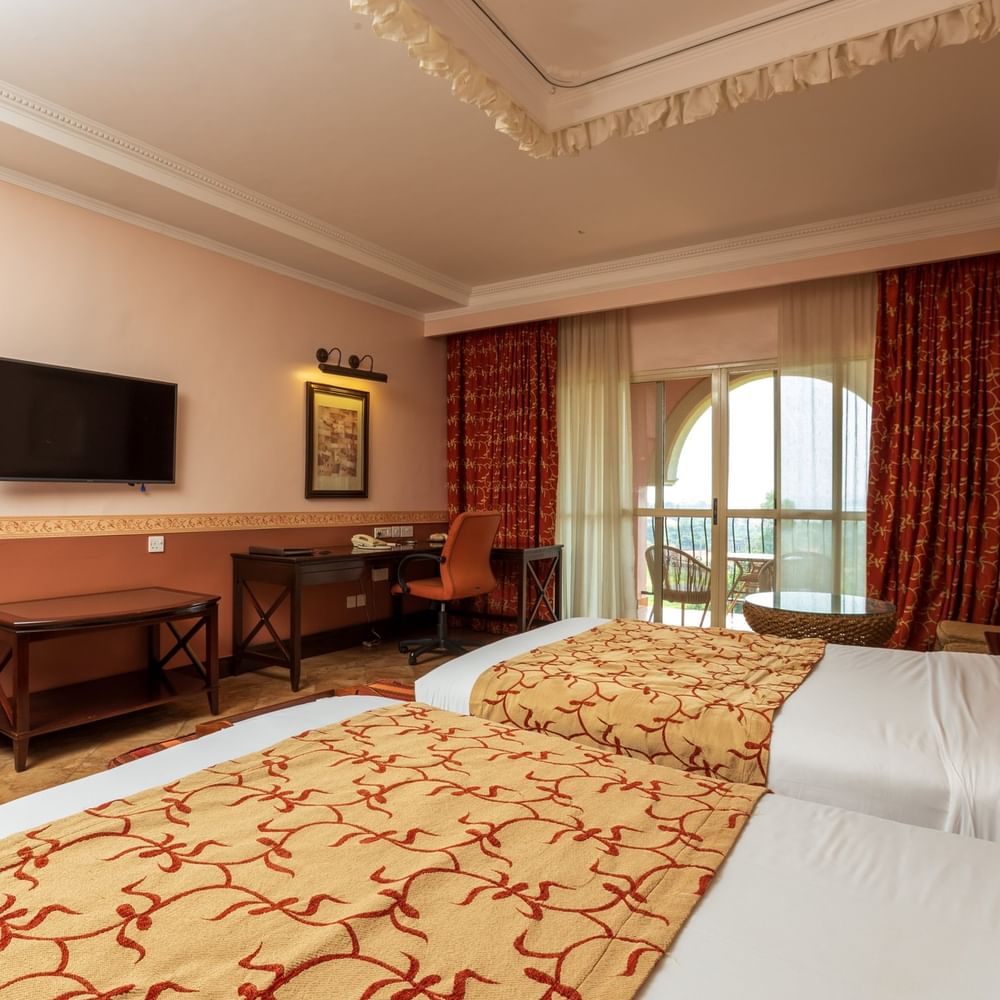 Two twin beds with patterned blankets and a balcony in a Standard Twin Room at Lake Victoria Serena Golf Resort & Spa, Kampala.