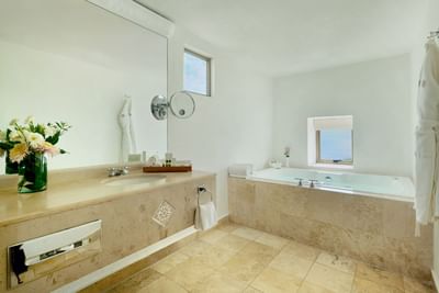 A bathroom with a large bathtub, sink, mirror, and decorative elements like flowers and towels.