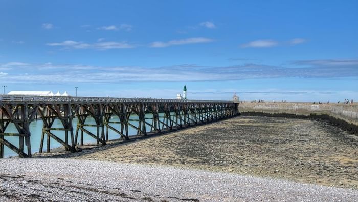 Vue sur la jetée en bois de la côte avec ciel bleu et phares en arrière-plan.