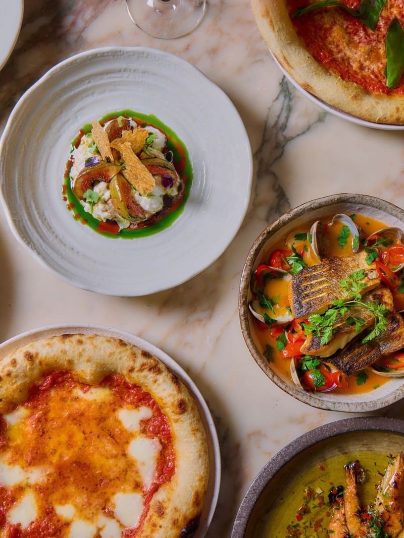 Assorted gourmet dishes from the A La Carte menu and two wine glasses on a marble table in the May Fair Kitchen