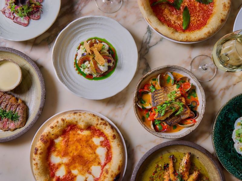 Assorted gourmet dishes from the A La Carte menu and two wine glasses on a marble table in the May Fair Kitchen