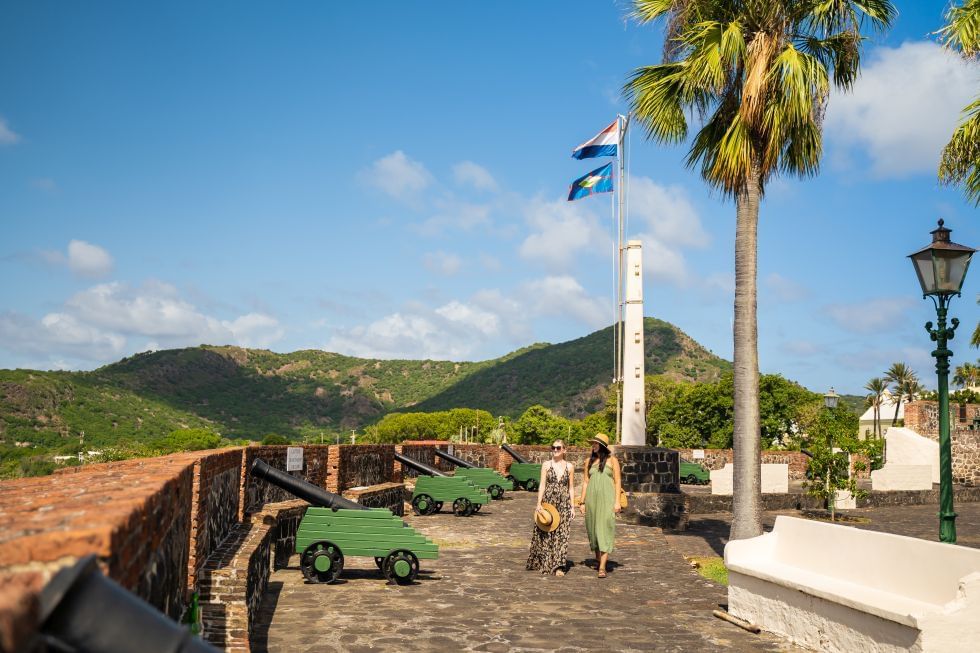 Two women walking through a historic fort in Oranje in St. Eustatius, with cannons & palm trees near Golden Rock Resort