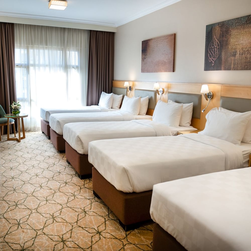 أربعة أسرّة مزودة بملاءات ووسائد بيضاء في غرفة فندقية في فندق سجى ورويك المدينة المنورة.