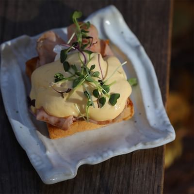 Piatto bianco con un sandwich di pane, prosciutto, uovo e erbe aromatiche su un tavolo di legno.