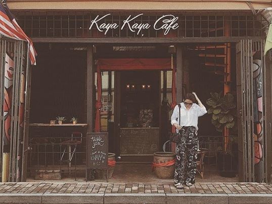 A woman in a white blouse and floral pants stands outside the Kaya Kaya Cafe entrance near YTL Hotels