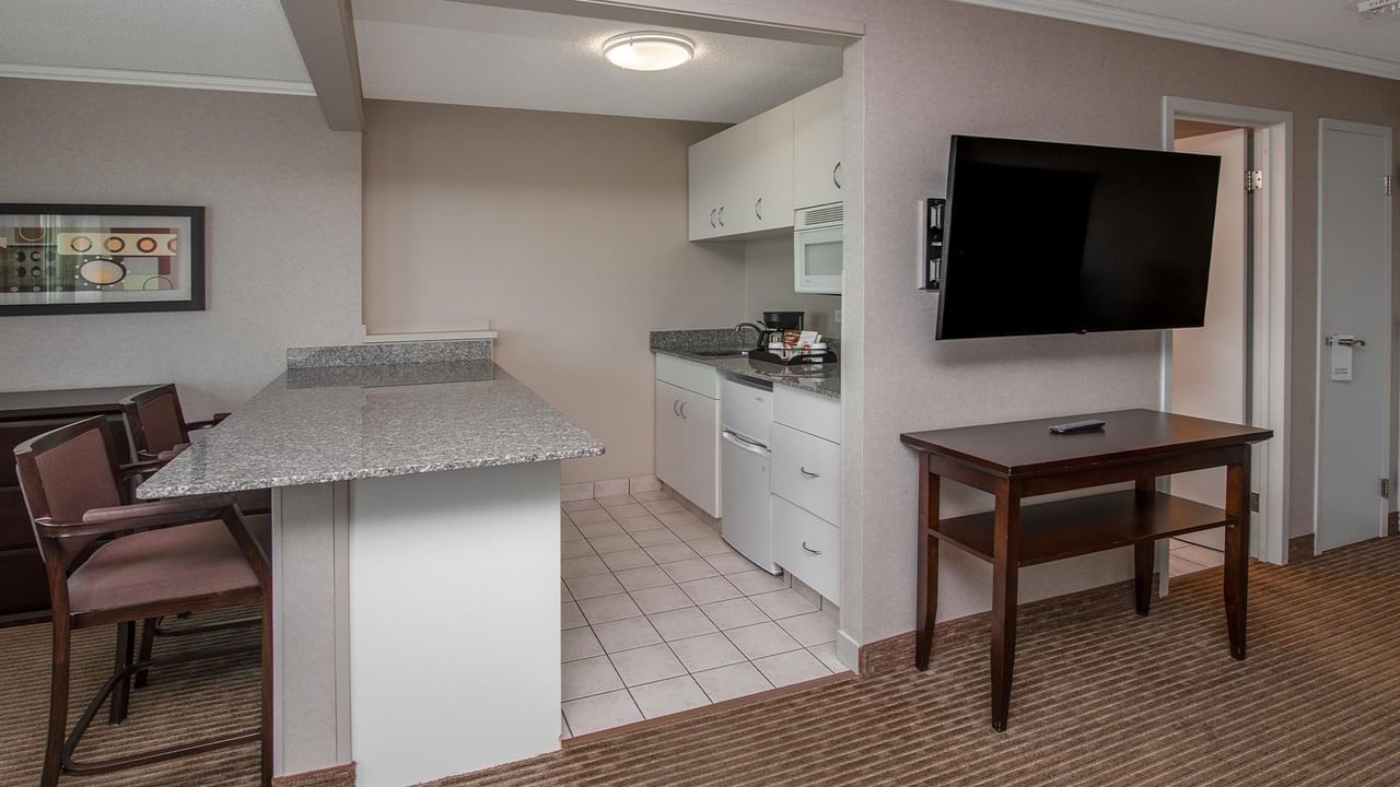 Hotel suite kitchen and dining area with a wall-mounted TV and small table.
