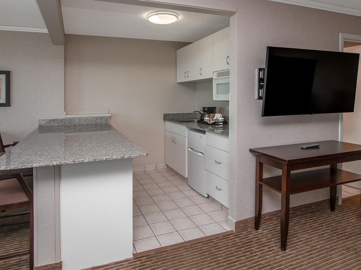 Hotel suite with a kitchenette, dining table, wall-mounted TV and sitting area.