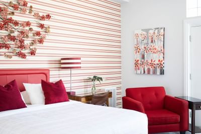 queen bed with red chair beside and red and white striped walls