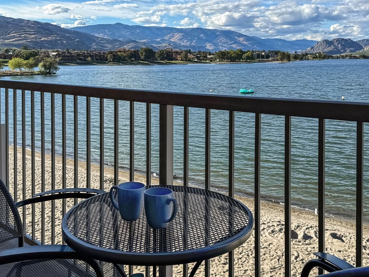 Balcony lake view with two chairs and coffee mugs.
