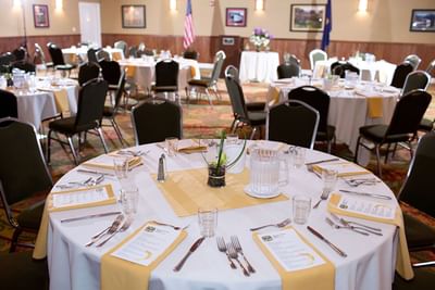 Round dining tables set with yellow napkins and green chairs, under bright lights in a hall at Cambria Pines Lodge