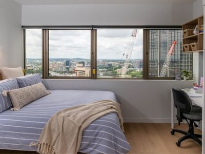 Modern bedroom with blue bedding, city view, and desk at UniLodge Brisbane City.