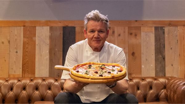 Chef Gordon Ramsay smiling and presenting a hot pizza topped with olives and basil at Sunway Resort