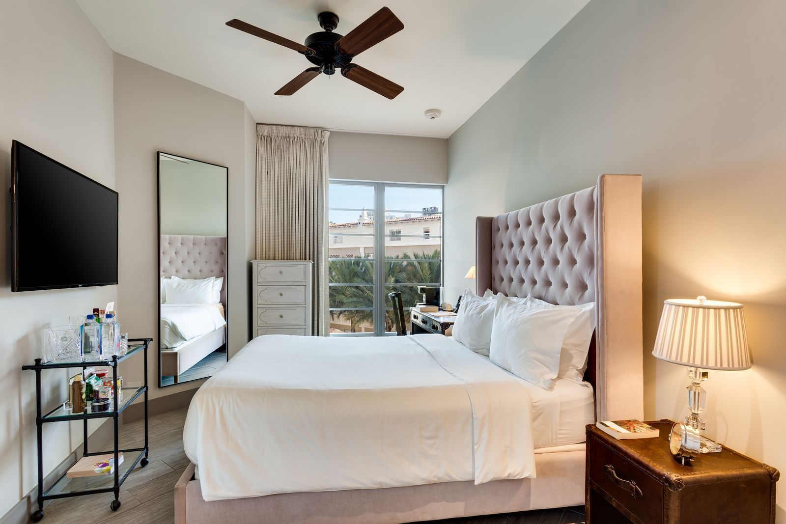 A wide view of a hotel room with a king-sized bed, ceiling fan, and flat-screen TV.
