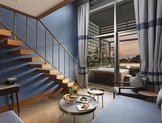 Titanic Deluxe Lara – Annex Duplex Suite’te mavi duvarlı, ahşap merdivenli ve balkonlu zarif bir oda.