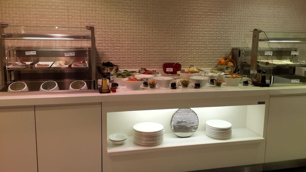 Salad bowls by stacks of white plates under a glowing display shelf in Breakfast & In-Room Dining at Warwick Ankara
