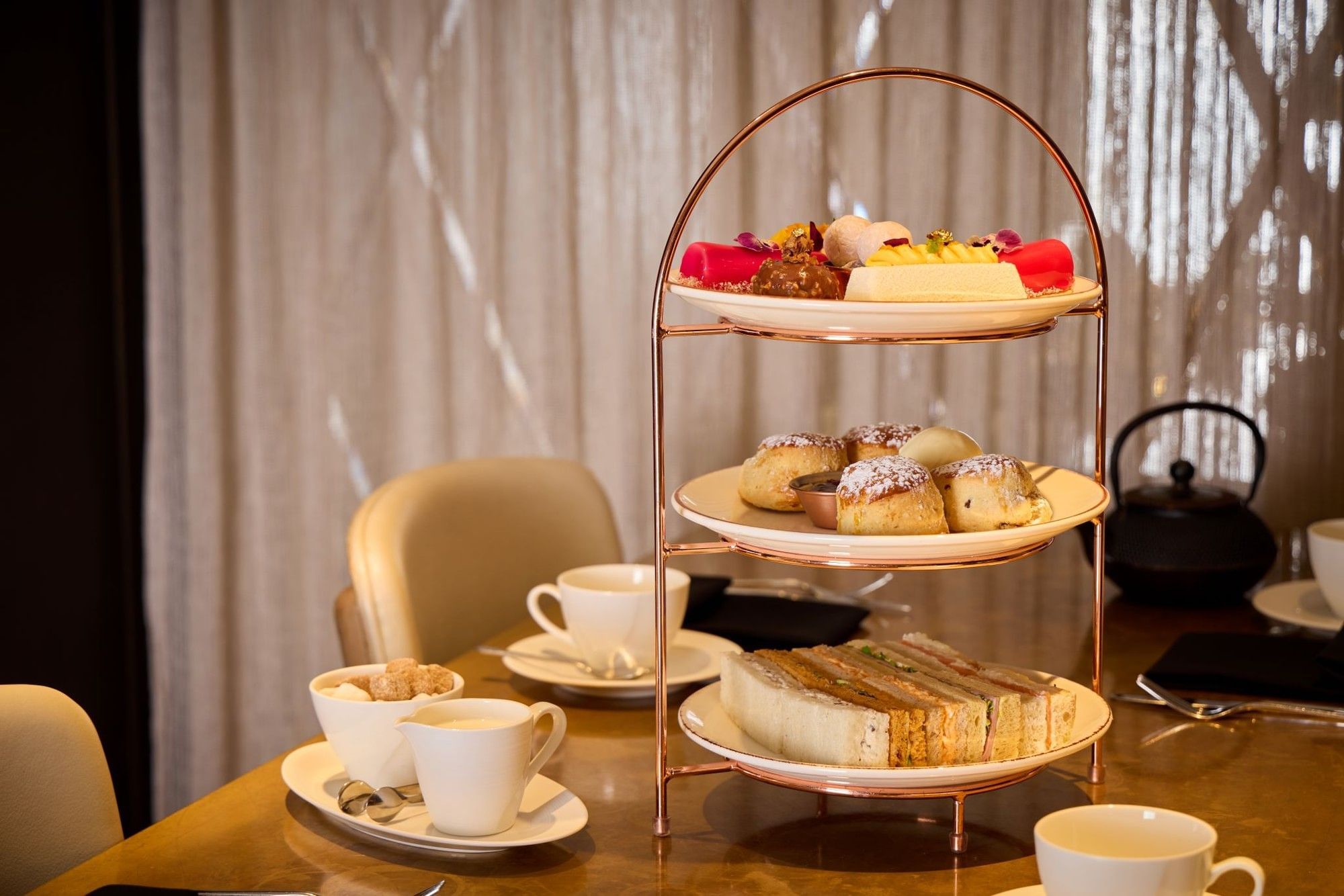 Three-tiered afternoon tea filled with pastries, scones, and sandwiches on a table at The May Fair Hotel