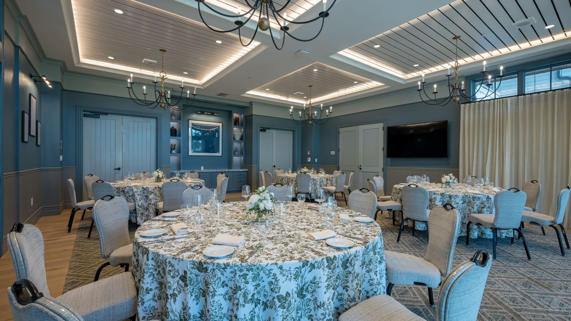 Club Room with elegant round tables, blue patterned linens, upholstered chairs, and chandeliers at Camp Creek Inn, Inlet Beach