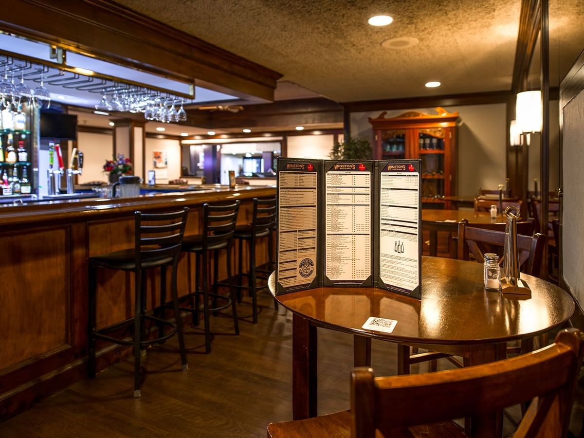 Interior of Winston's Resto-Bar with wooden furniture, a menu on a table, and shelves stocked with bottles.