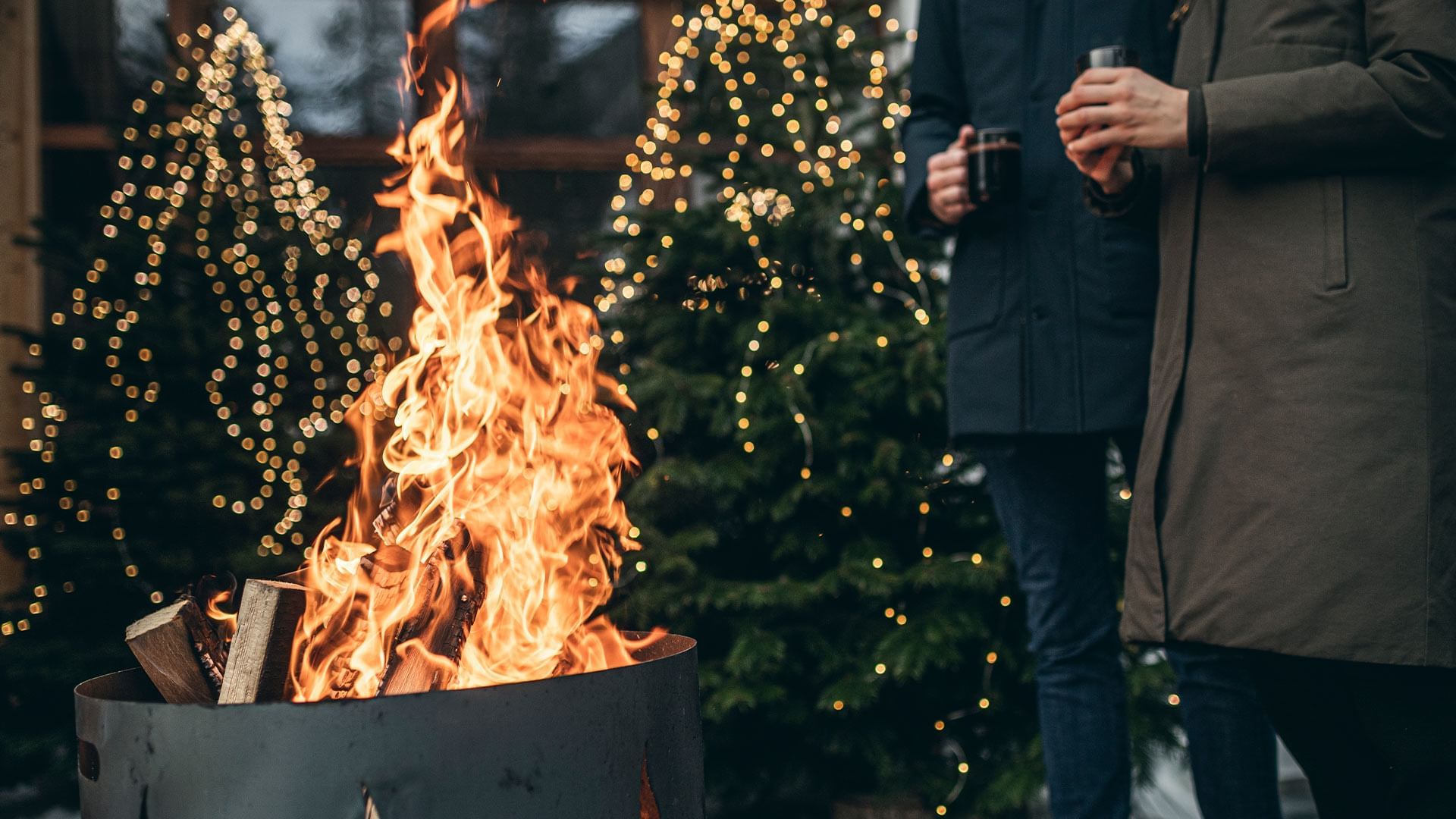 Flames engulfing a metal container with blurred Christmas light backdrop at Falkensteiner Hotels & Residences