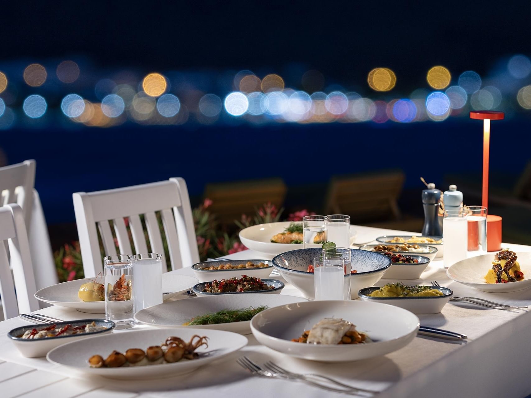 A dinner table at Titanic Luxury Collection Bodrum, overlooking the illuminated cityscape at night.