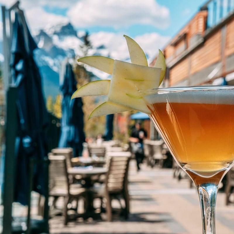 Close-up of a garnished martini cocktail on a mountain-view patio at Spring Creek Resorts, featuring Canmore events