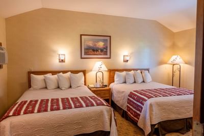 Nightstand by the cozy beds in Aspen Cabins with warm lighting and carpeted floors at The Ranch at UCross