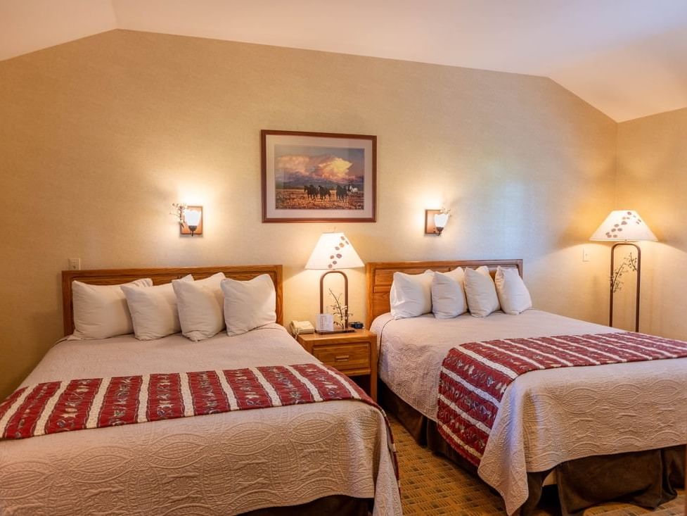 Nightstand by the cozy beds in Aspen Cabins with warm lighting and carpeted floors at The Ranch at UCross