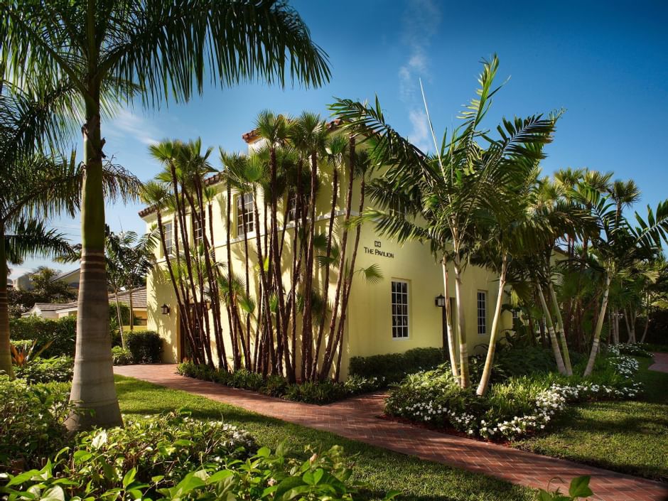Yellow two-story Pavilion building behind tall palm trees along brick pathway under blue sky at The Brazilian Court