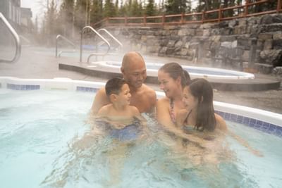 Family enjoying a relaxing soak in a hot tub surrounded by steaming water and scenic greenery at Blackstone Mountain Lodge