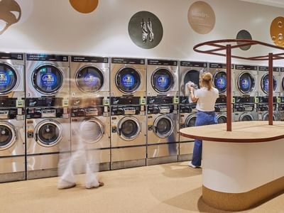 Woman standing behind a counter in a laundromat, while another woman walks by in a blur.
