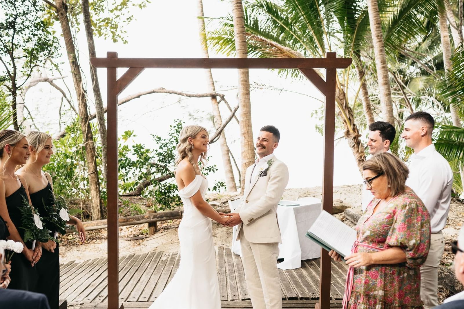 Outdoor wedding with bride and groom under wooden frame & guests watching at Pullman Port Douglas Sea Temple Resort & Spa