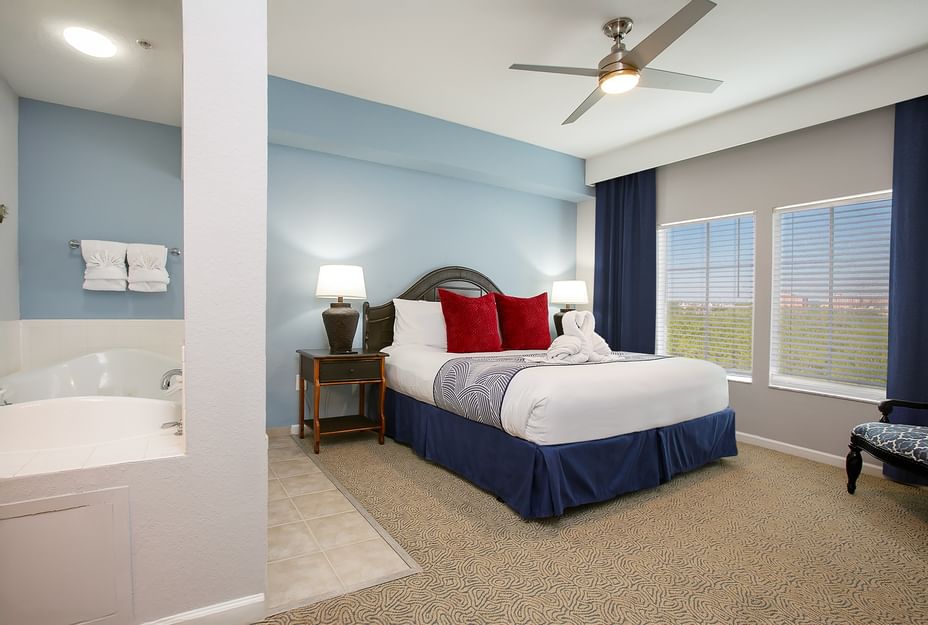 A hotel room with a bed, nightstand, lamp, ceiling fan, and window with blinds