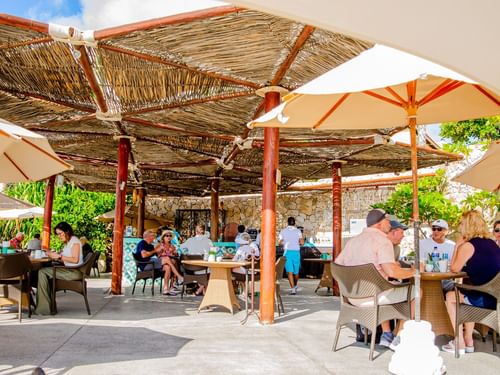 Outdoor seating area with people dining under thatched shade structure in Tortugas restaurant at Hacienda del Mar Los Cabos